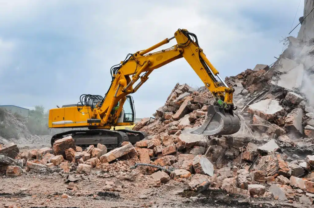 Yellow excavator clearing large pile of construction debris